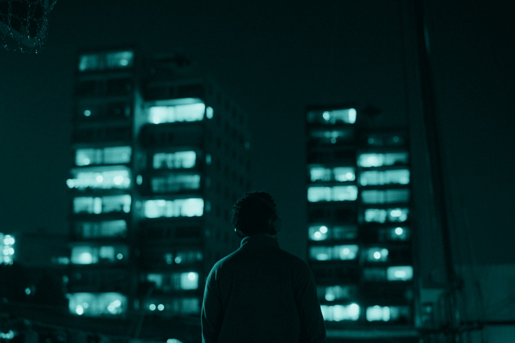 A person listening to music, facing the turquoise lights of the city